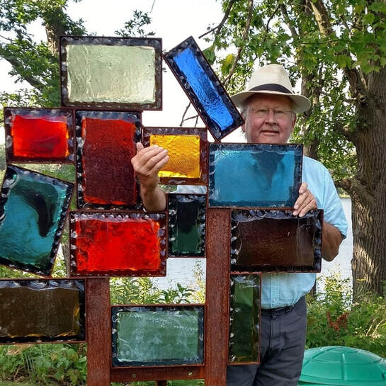 Frank Stone holding a stained glass installation outdoors
